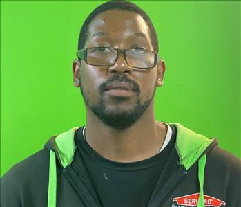male SERVPRO employee with glasses in uniform in front of green background